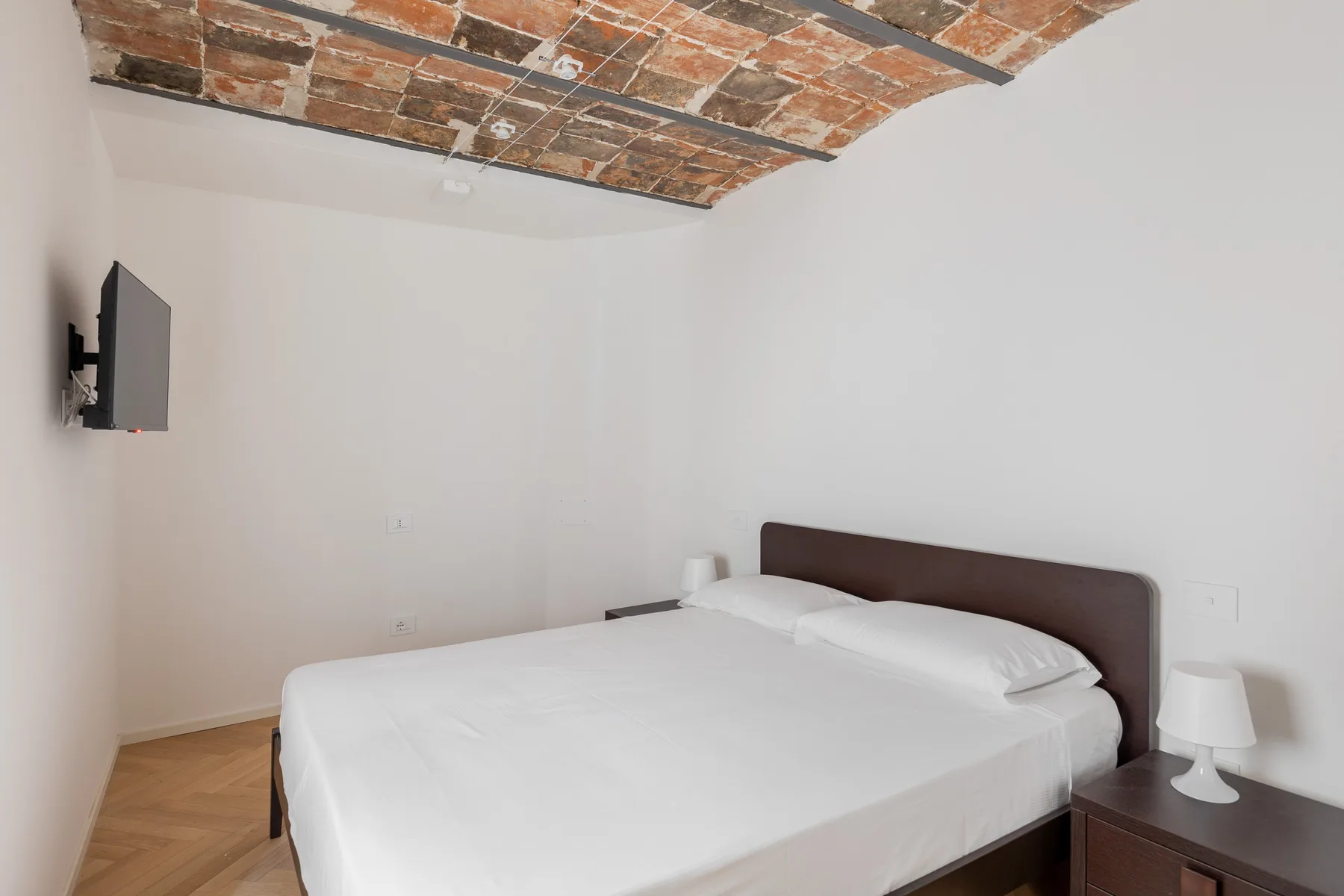 A bedroom with a neatly made bed beneath a brick ceiling.