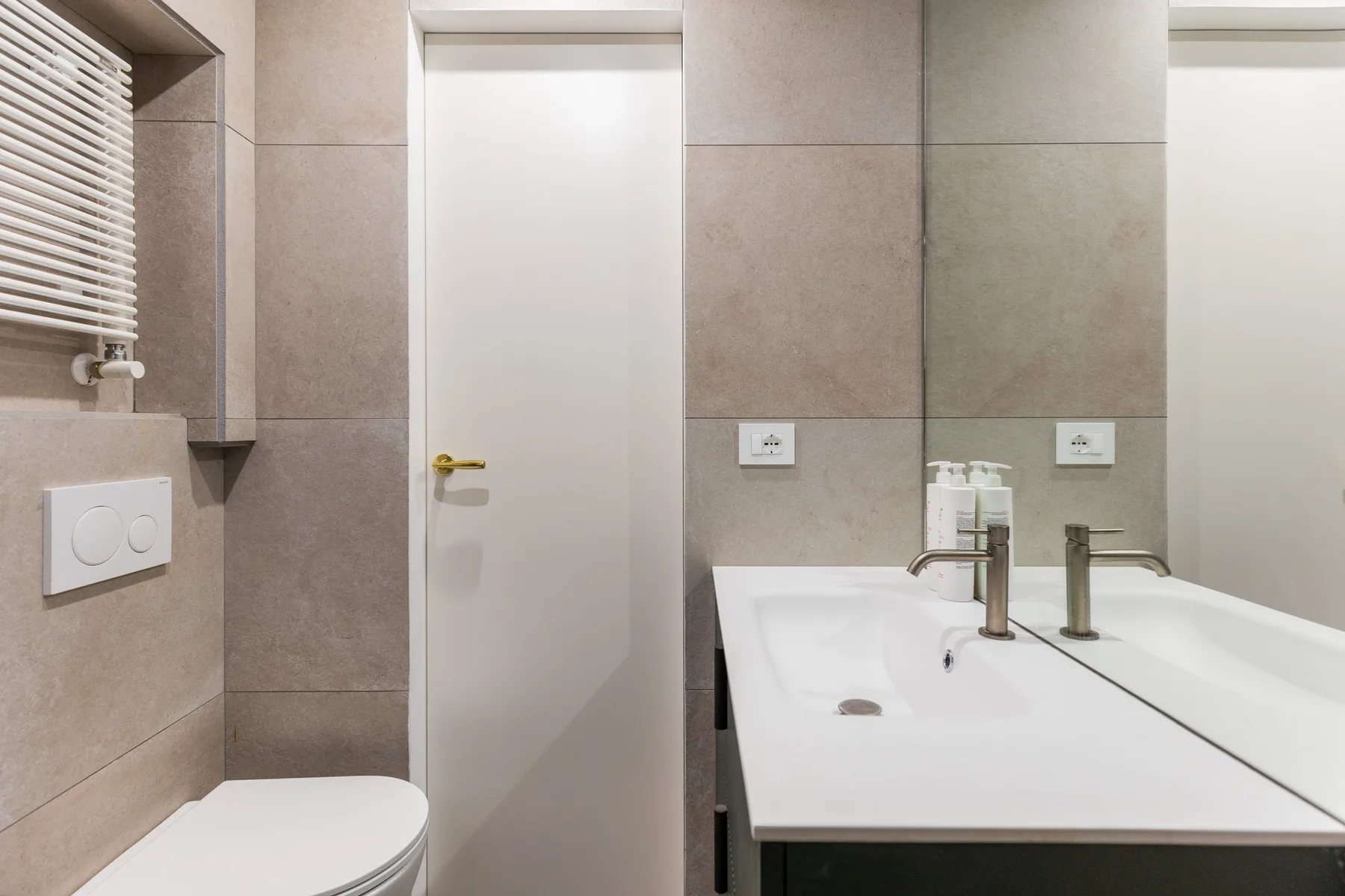 A tiled bathroom with a white sink, mirror, and closed door.