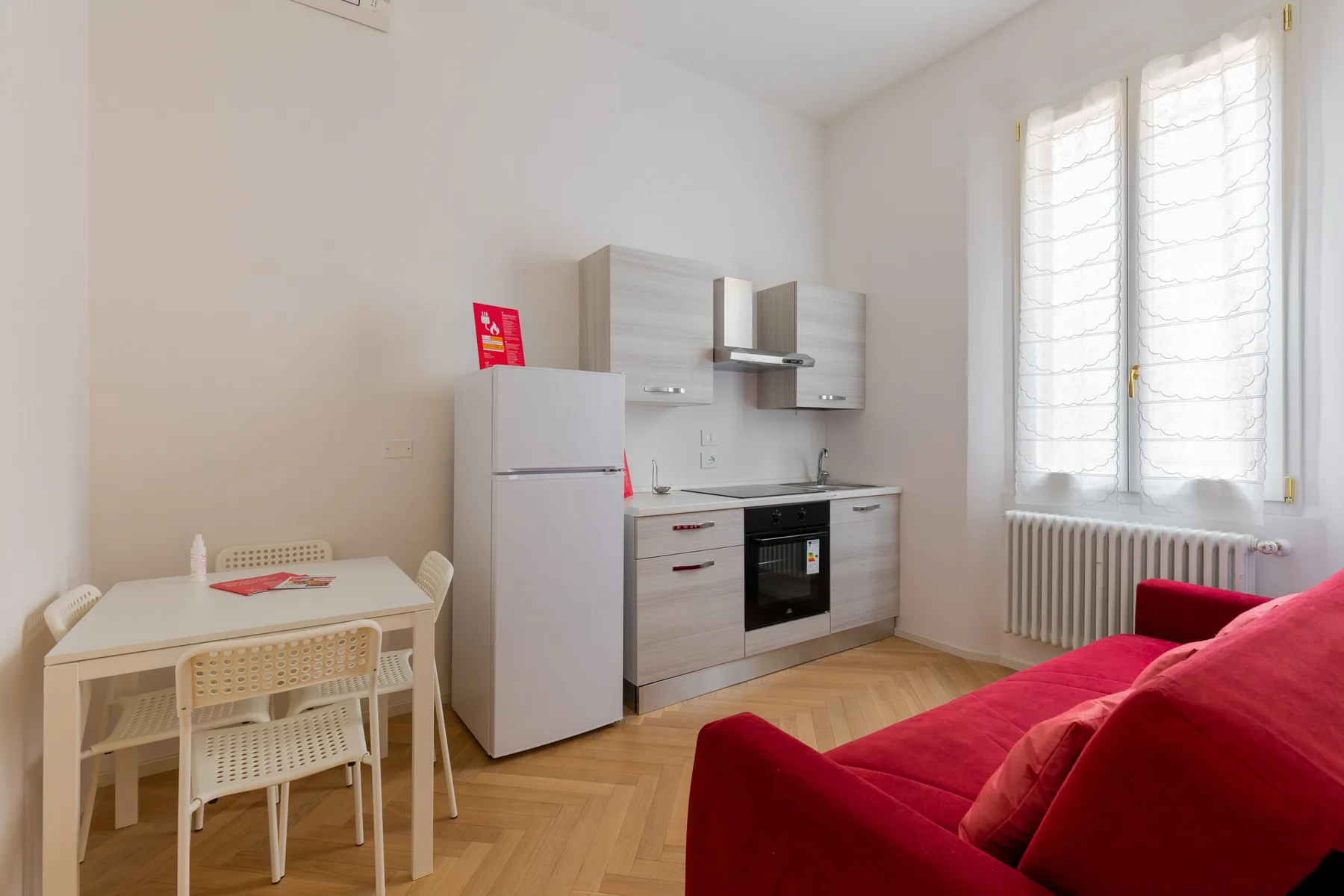 A compact kitchen and dining area with a red sofa beside the window.