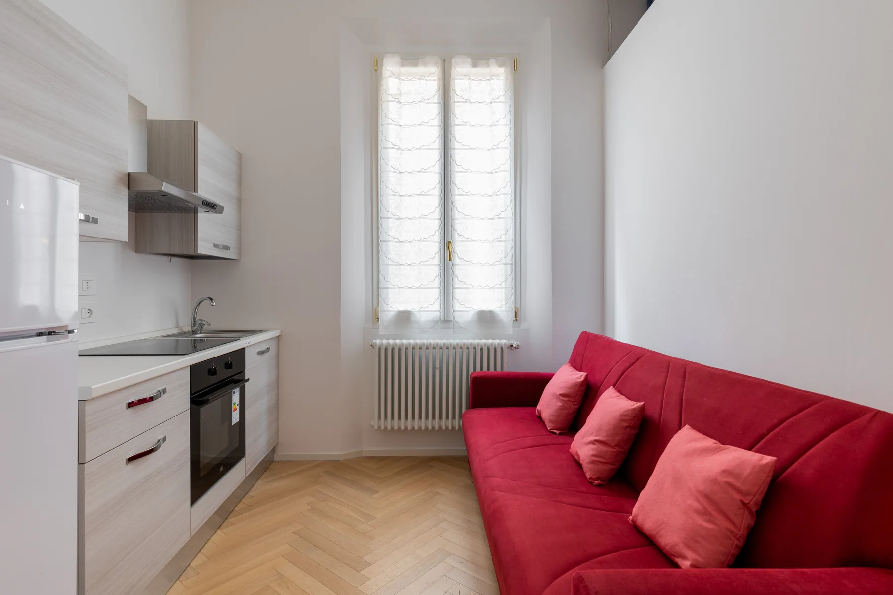 A compact living area with a red sofa beside a small kitchen.