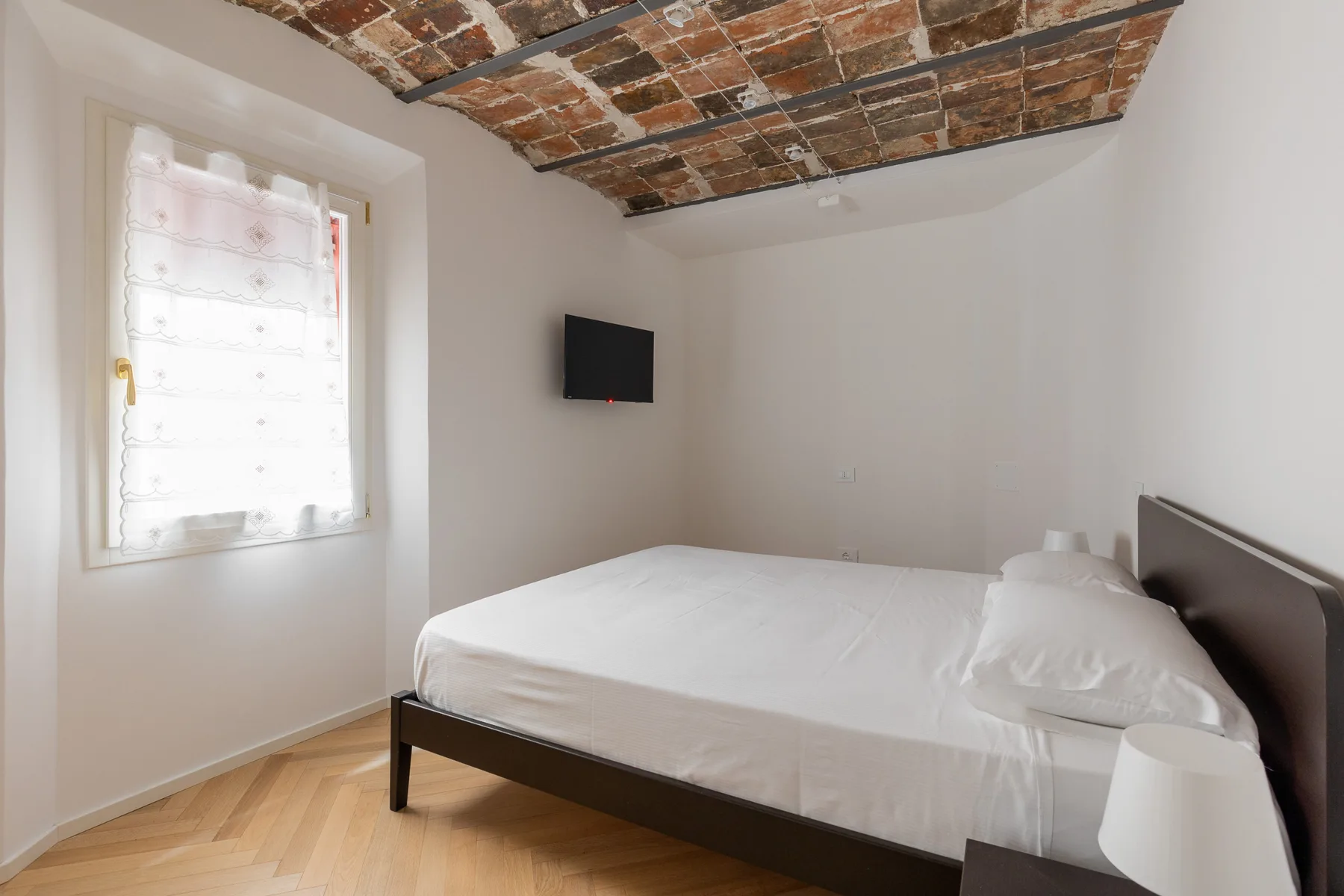 A bedroom with a bed, a window, and a television on the wall.