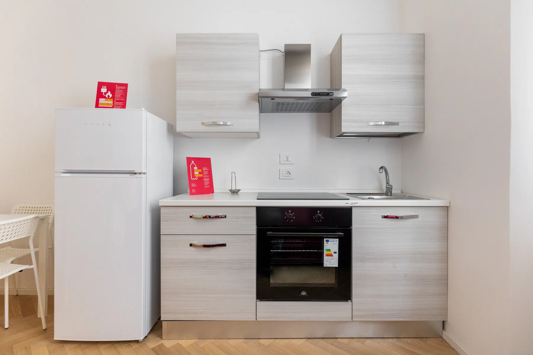 A compact kitchen with pale cabinets, a refrigerator, and a built-in oven.