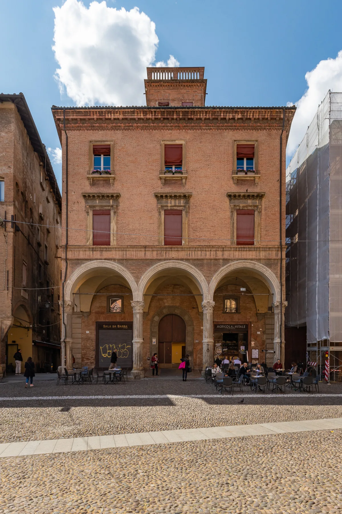 A brick building with arched ground-floor openings faces a broad cobblestone square.