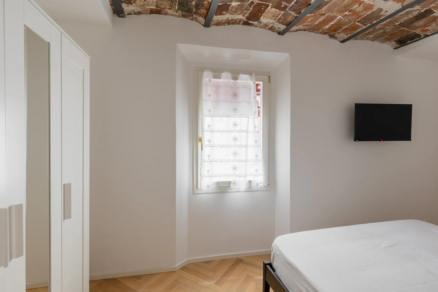 A bedroom with a bed, a window, and a wall-mounted television.