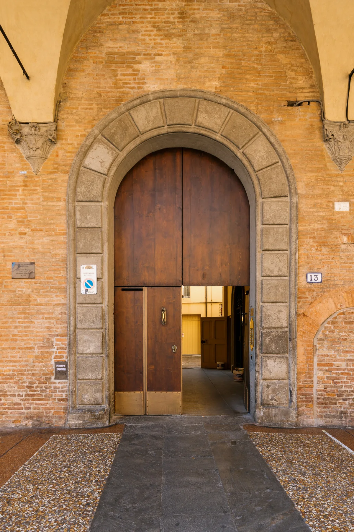 A tall wooden doorway sits within a rounded stone arch in a brick wall.