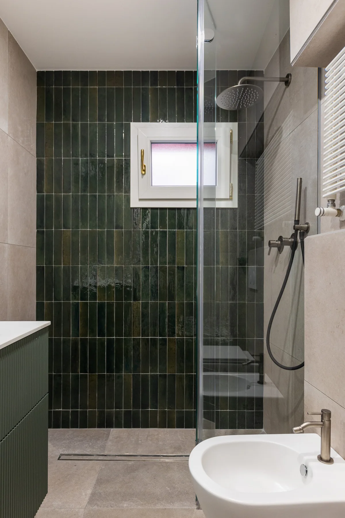 A tiled bathroom with a glass shower, wall-mounted showerhead, and sink.