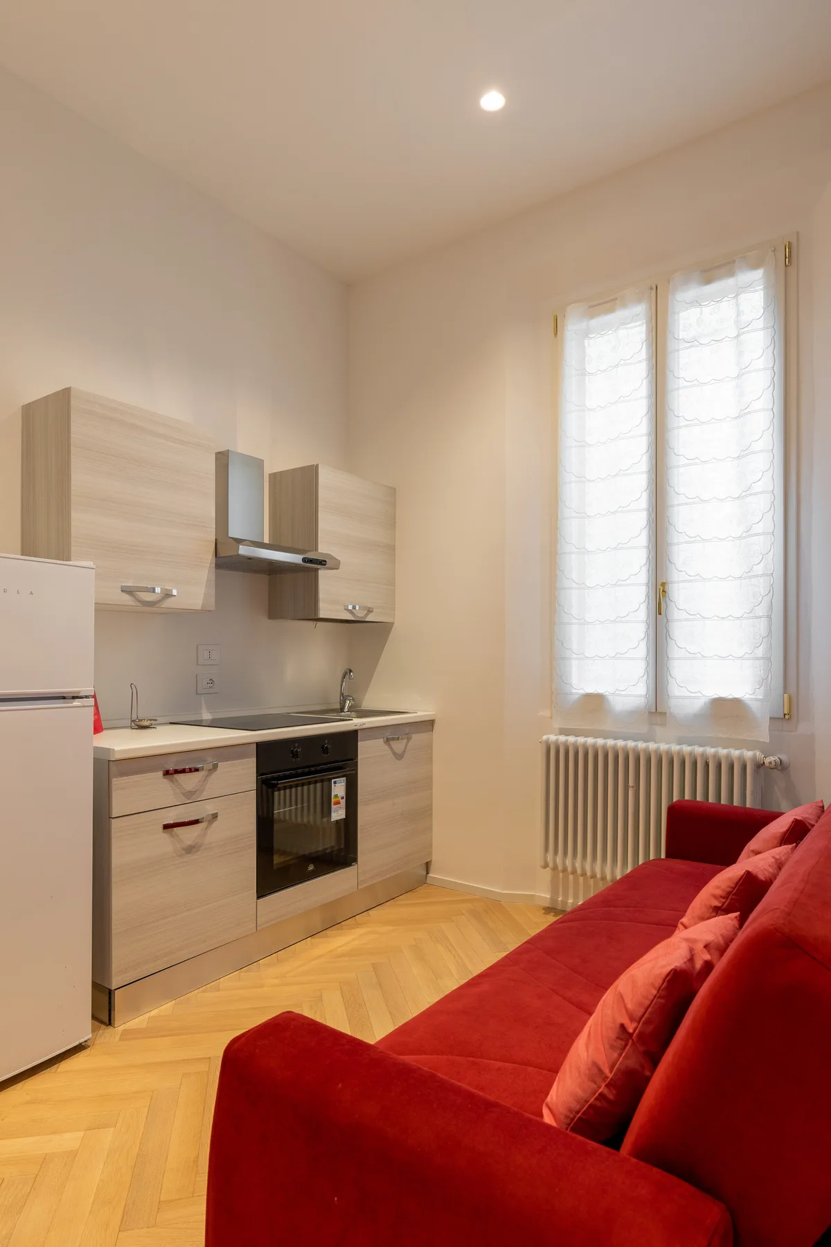 A compact kitchen and red seating share a bright room with a tall window.
