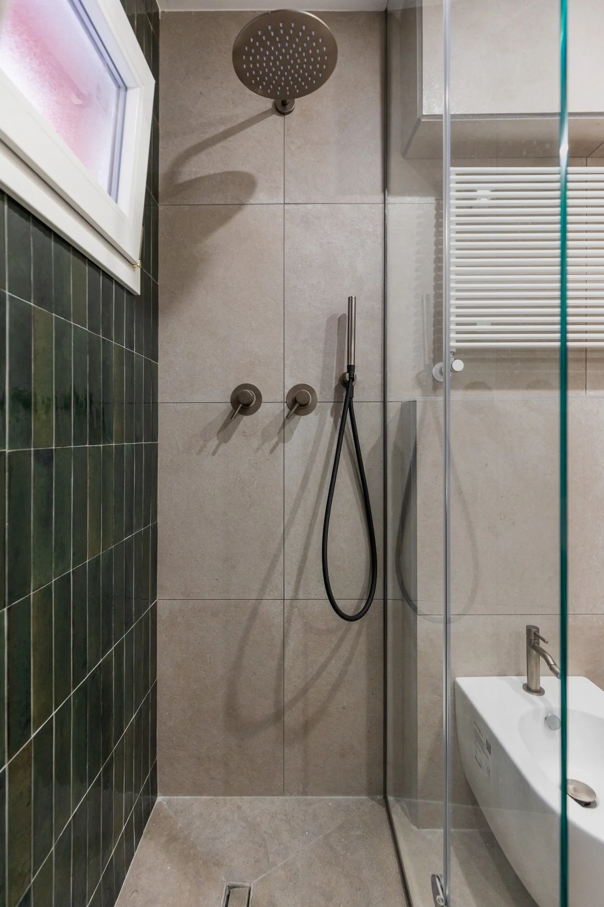 A tiled bathroom shower with a glass screen and handheld showerhead.