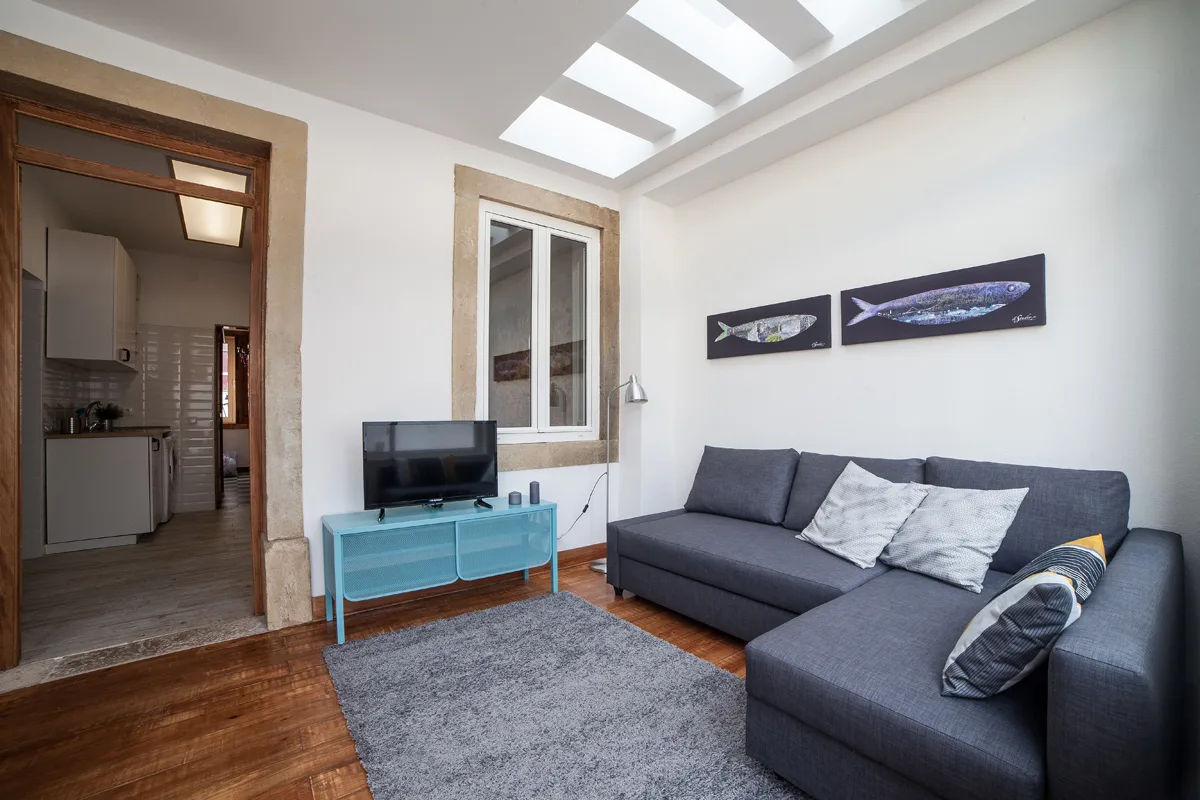 A living room with gray seating, a television, and a skylight.