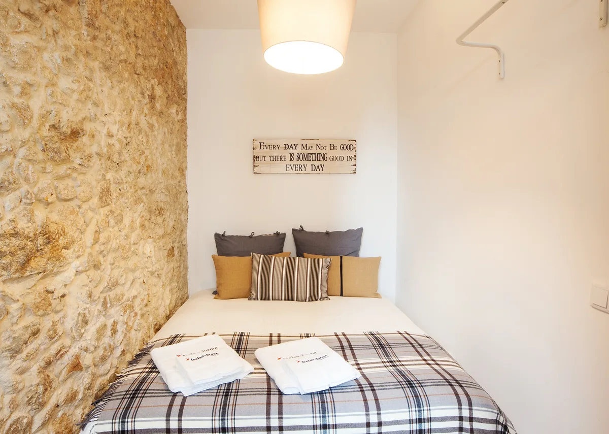 A bedroom with a double bed, plaid bedding, and a stone wall.