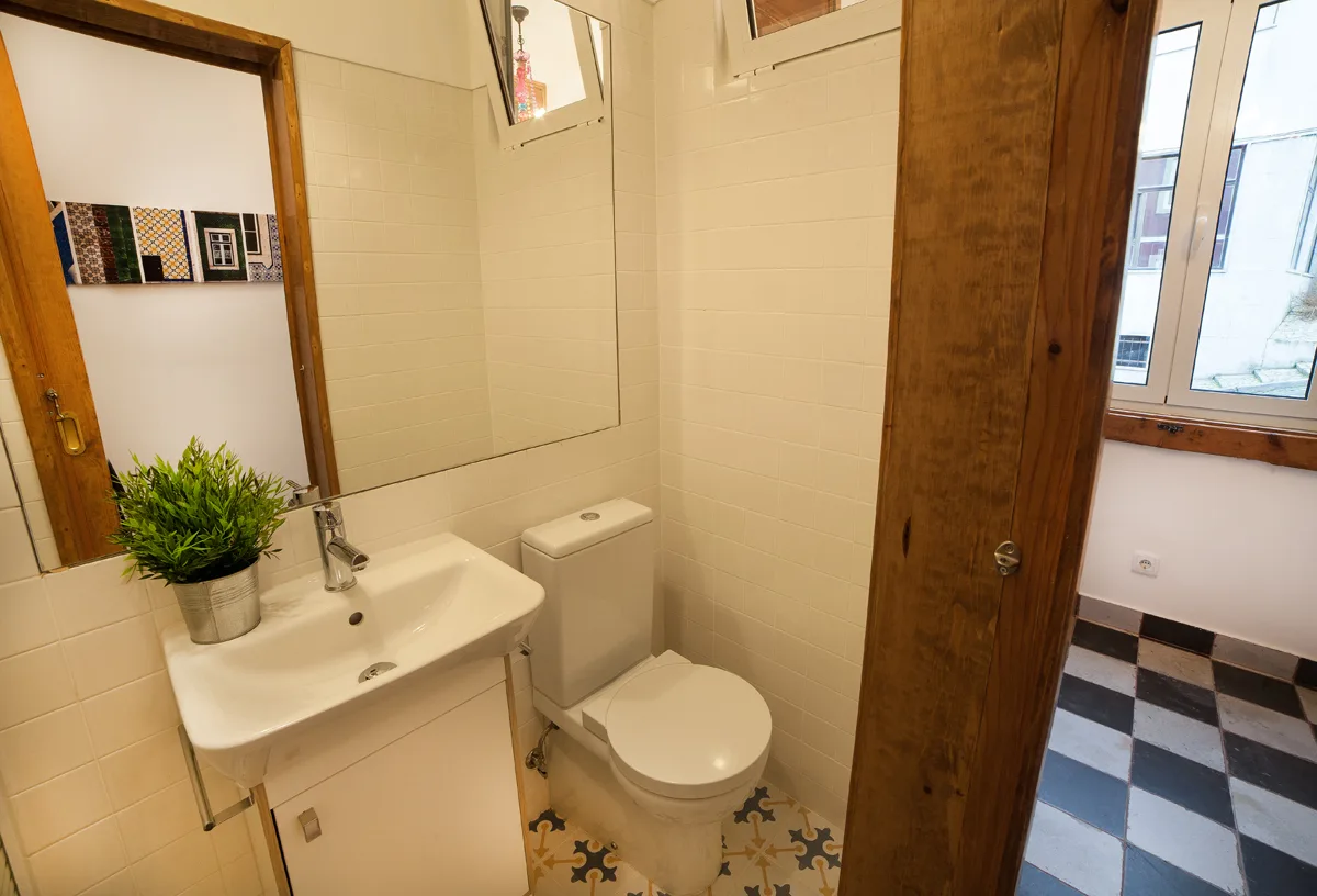 A bathroom with a sink and toilet, beside a windowed room.