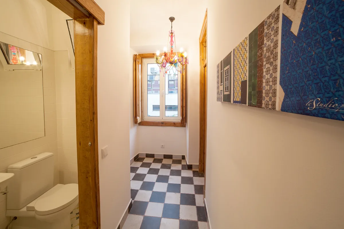 A narrow hallway with a checkered floor leads to a window.