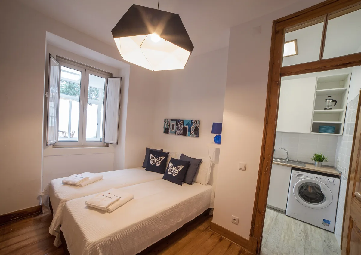 A bedroom with a bed beside a window and an open doorway to a laundry area.