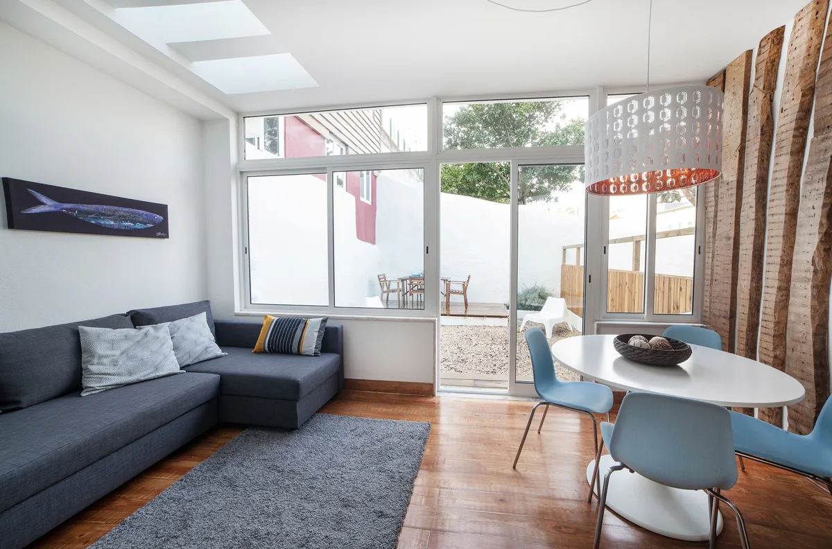 A bright living and dining area with seating beside large windows opening onto a patio.