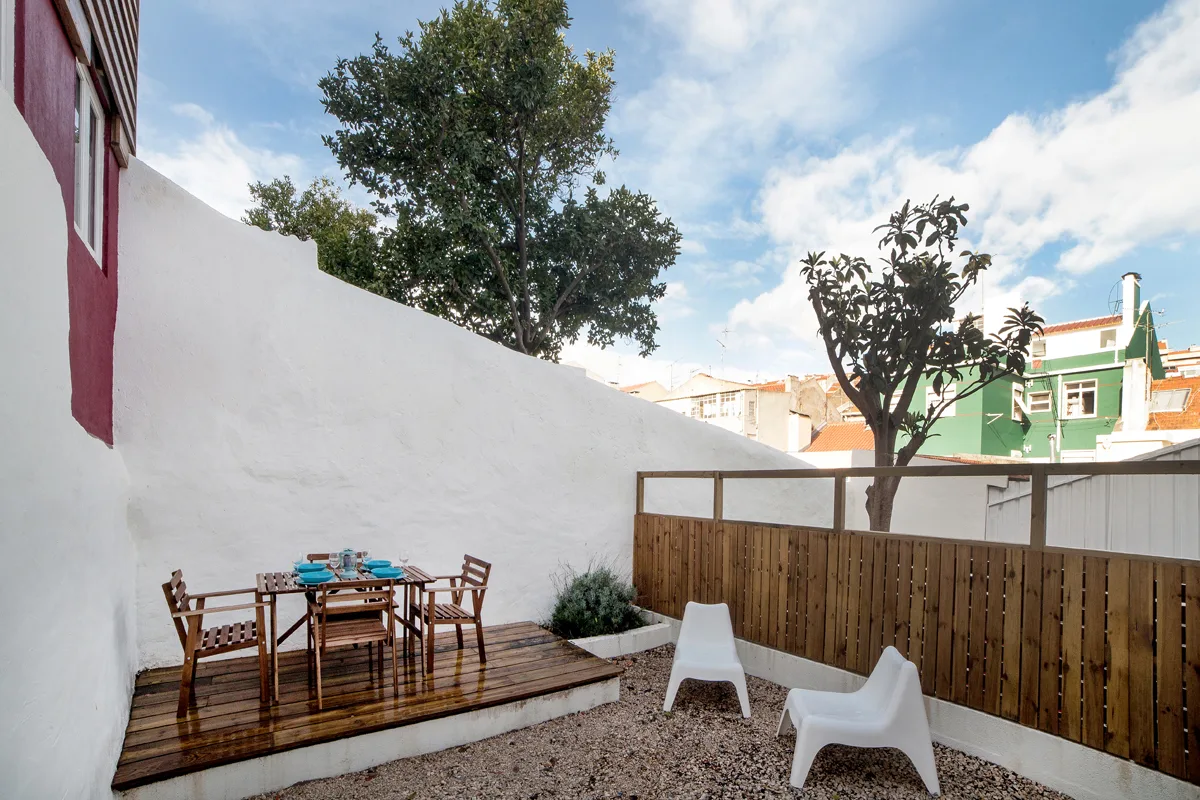 An outdoor patio with a wooden dining set, white seating, and trees.