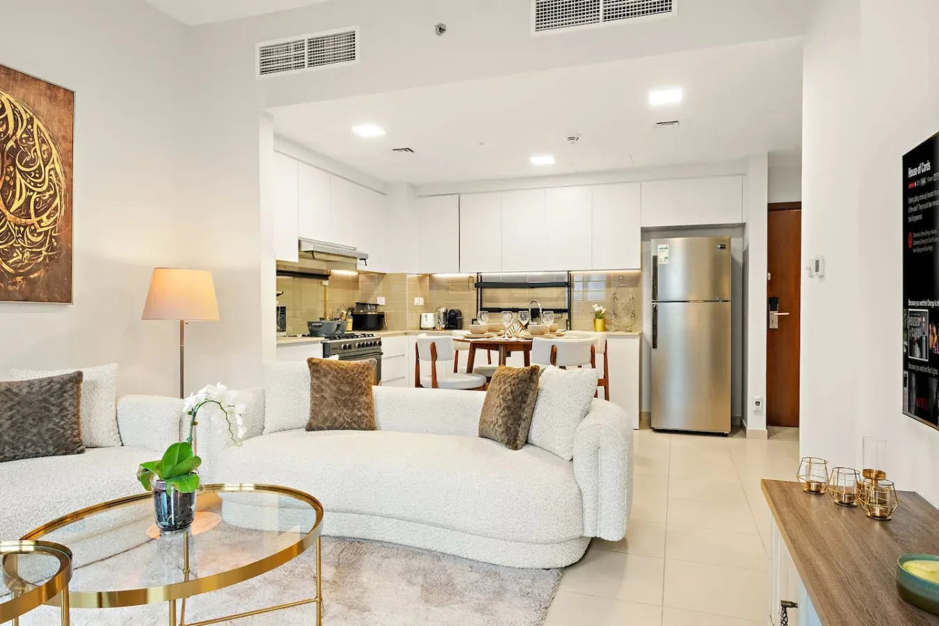 A bright living area opens onto a modern kitchen, with a light-colored sofa in front.