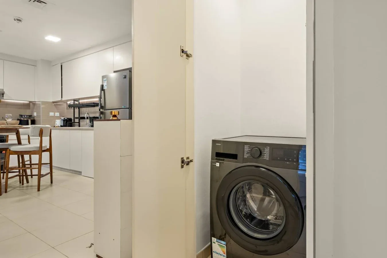 A washing machine stands beside a bright kitchen and dining area.