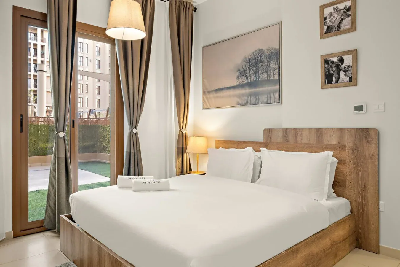 A bedroom with a neatly made bed beside tall curtained windows.
