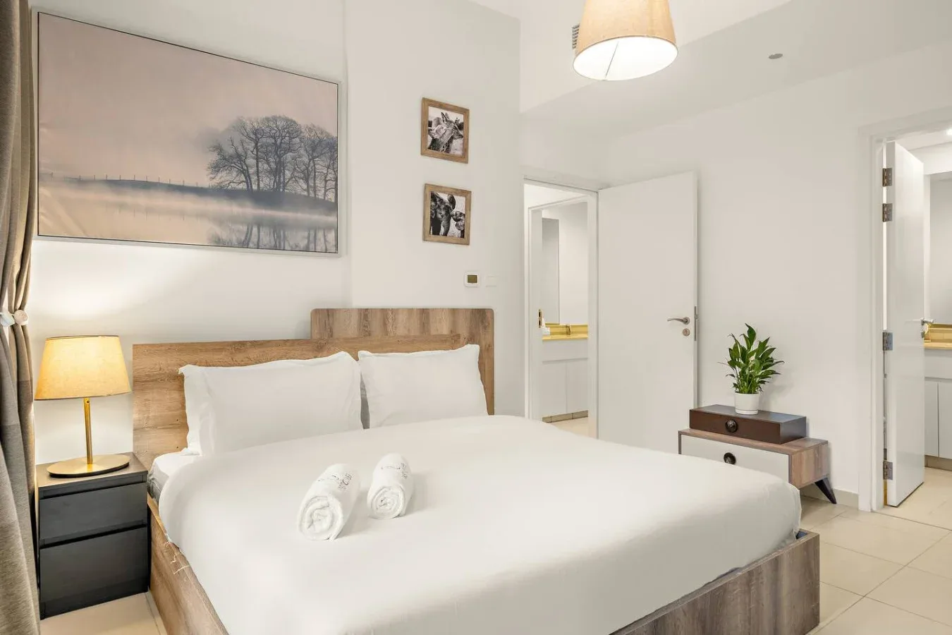 A bright bedroom features a neatly made bed and framed wall art.