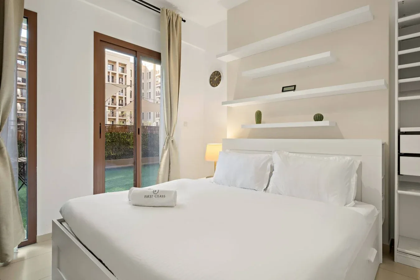 A bright bedroom with white bedding and glass doors opening onto a balcony.