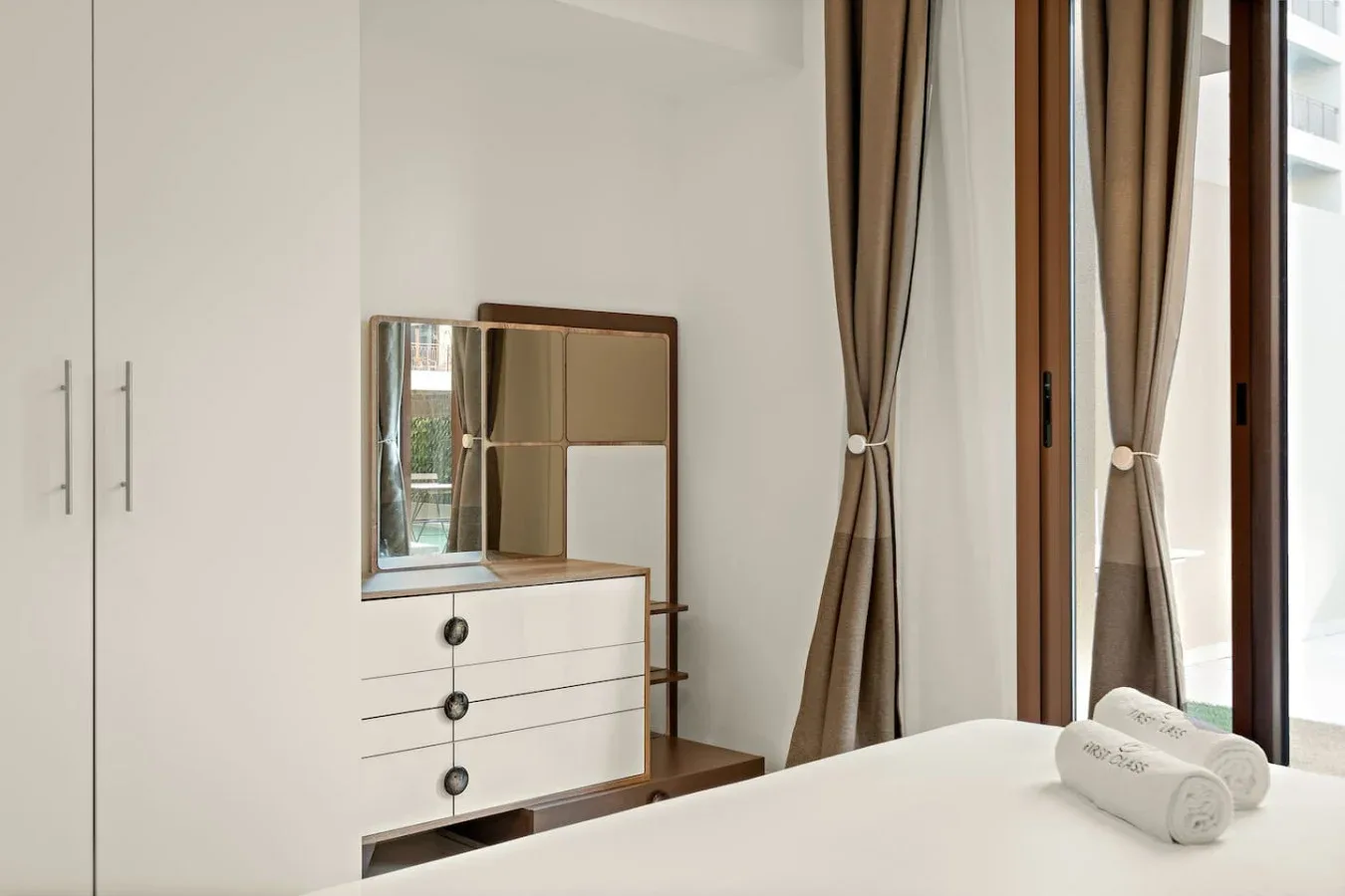 A bedroom with a dresser and mirror beside tall curtained windows.