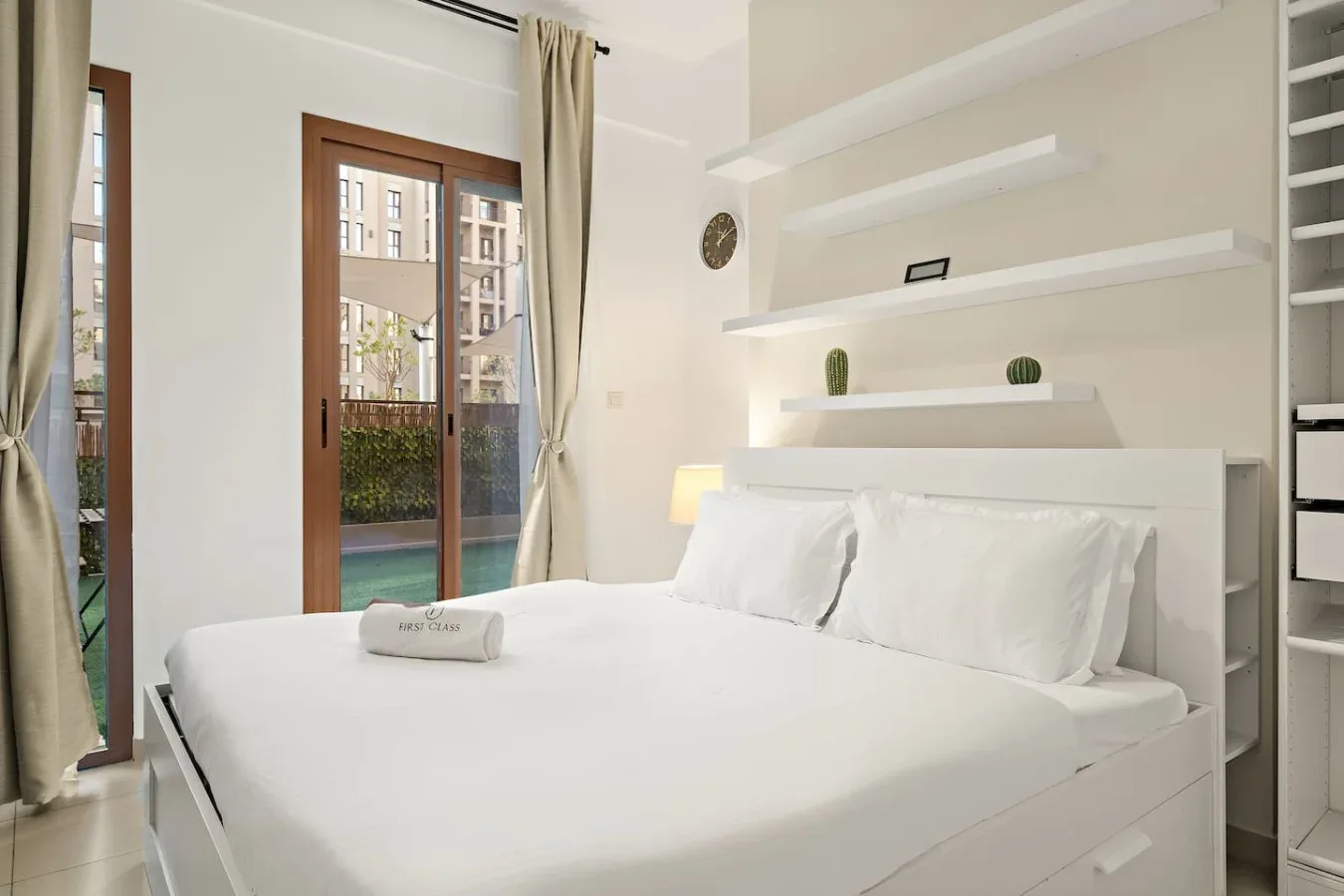 A bright bedroom with a neatly made bed beside tall windows.