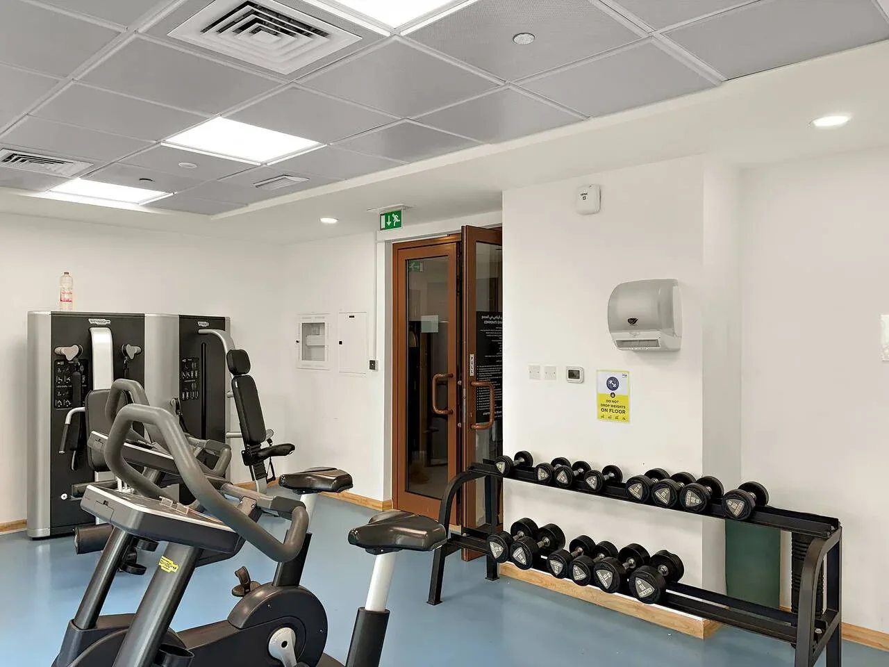 A gym with exercise machines, benches, and dumbbells along the wall.