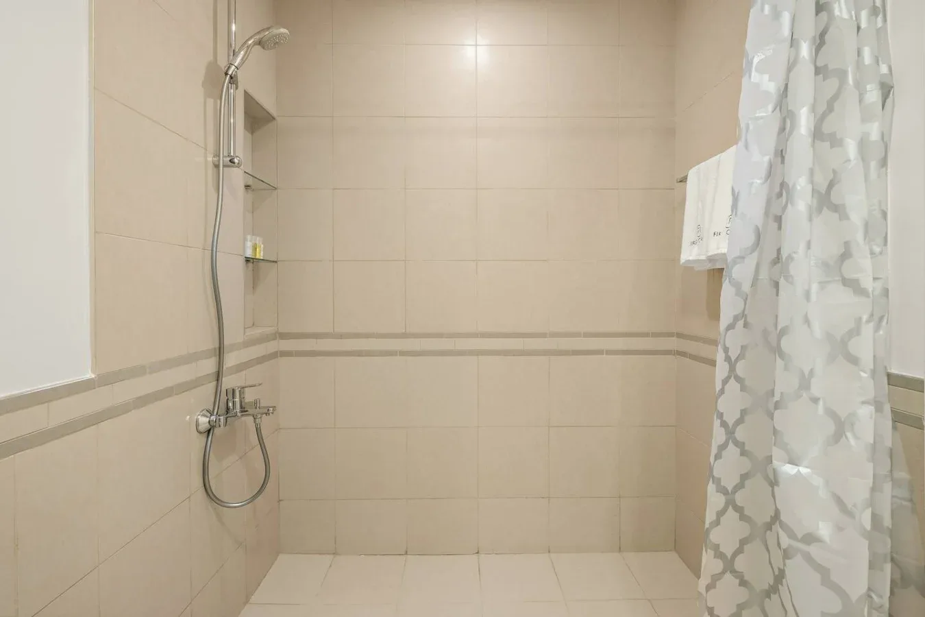 A tiled bathroom shower with a patterned curtain and wall-mounted showerhead.