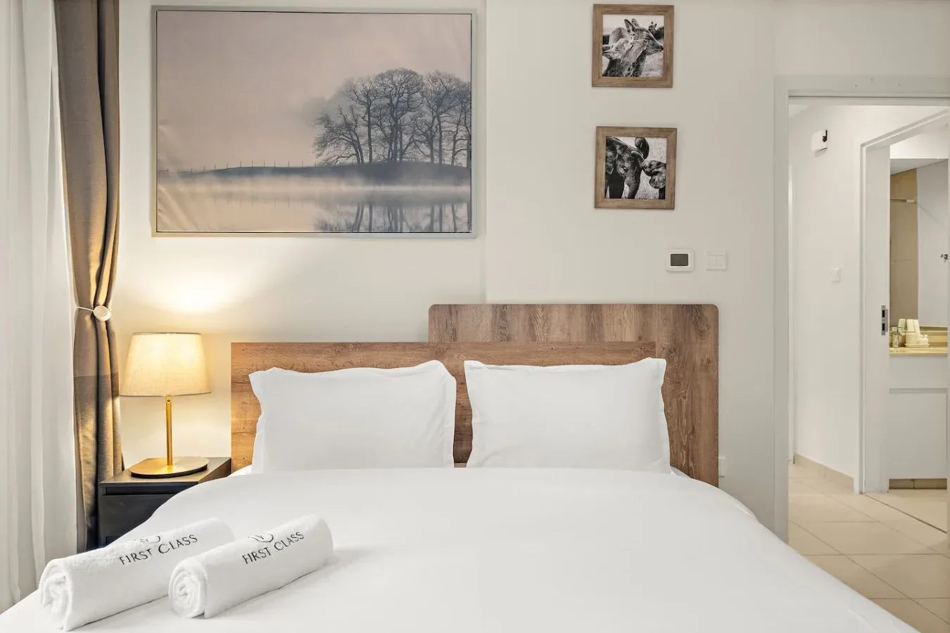 A bedroom with a neatly made bed, bedside lamp, and framed artwork.