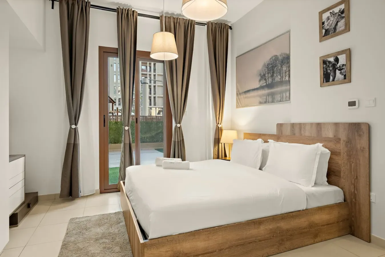 A bedroom with a wooden bed, white bedding, and tall curtained windows.