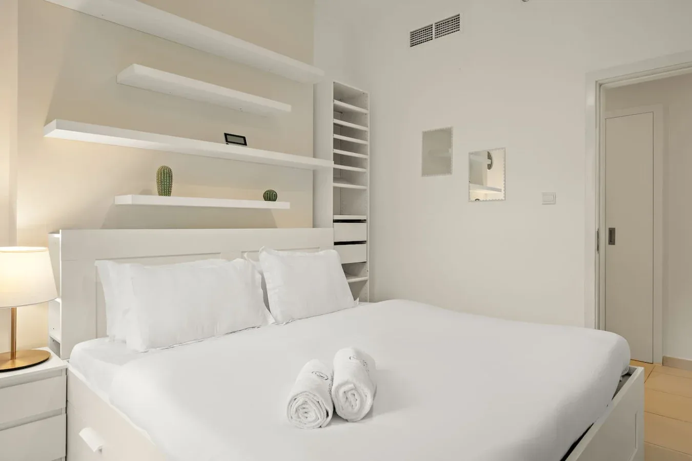 A bright bedroom with white bedding and built-in shelves behind the bed.