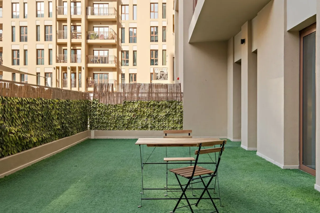 A small outdoor patio with green flooring and a table with chairs.