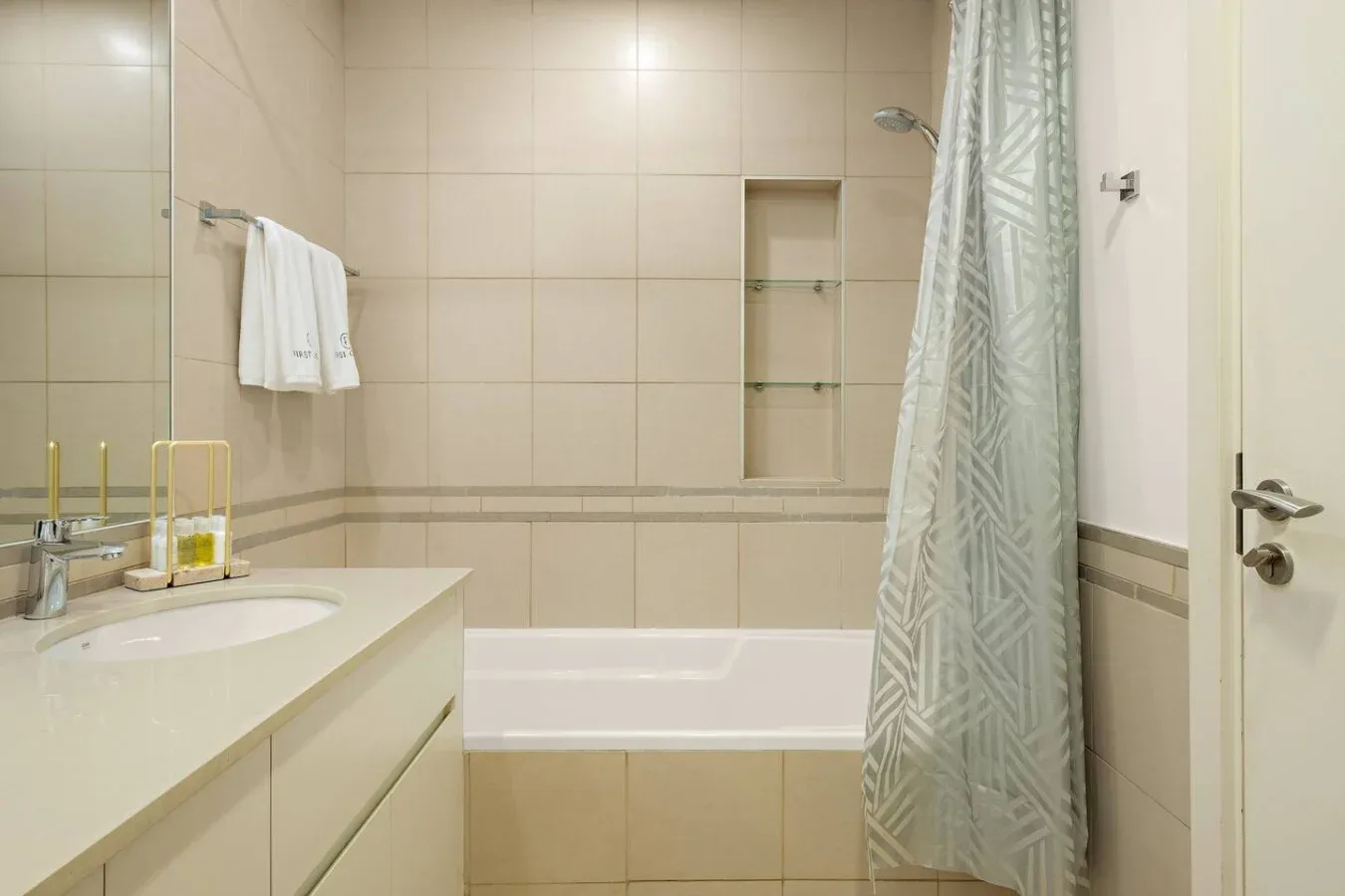 A tiled bathroom with a bathtub, shower curtain, and sink vanity.
