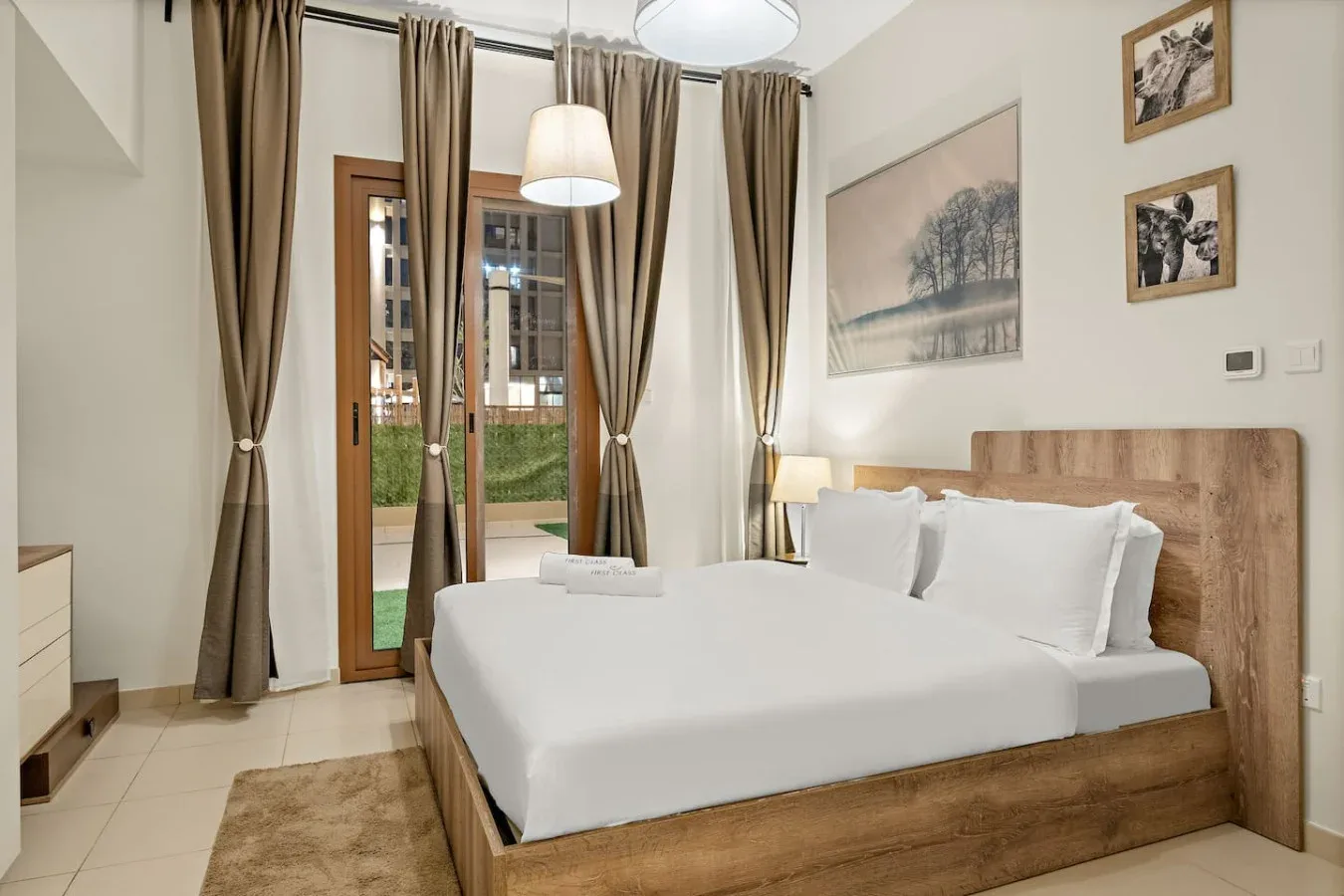 A bedroom with a neatly made bed, tall windows, and curtains.