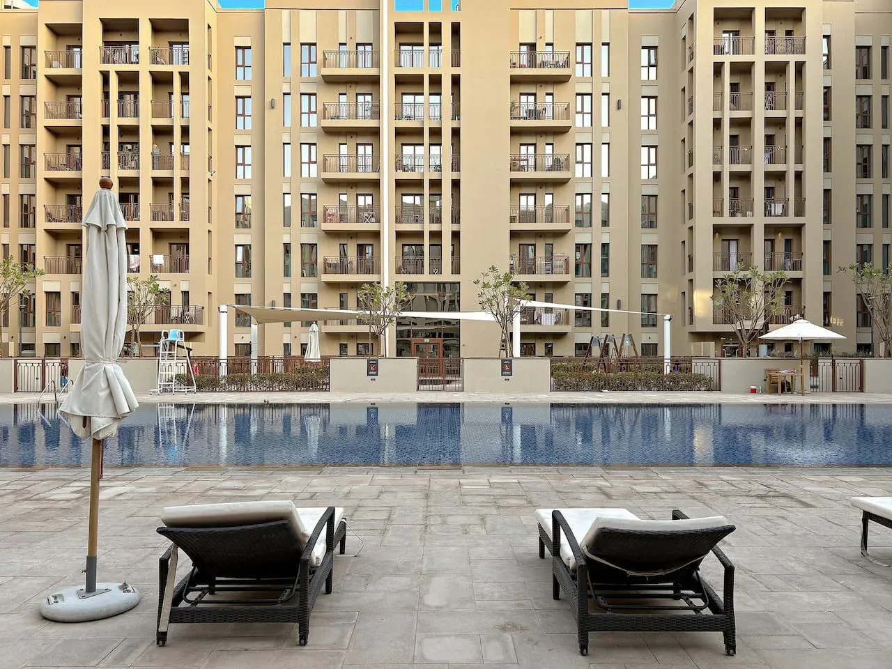 An outdoor swimming pool and paved deck sit in front of a multi-story building.