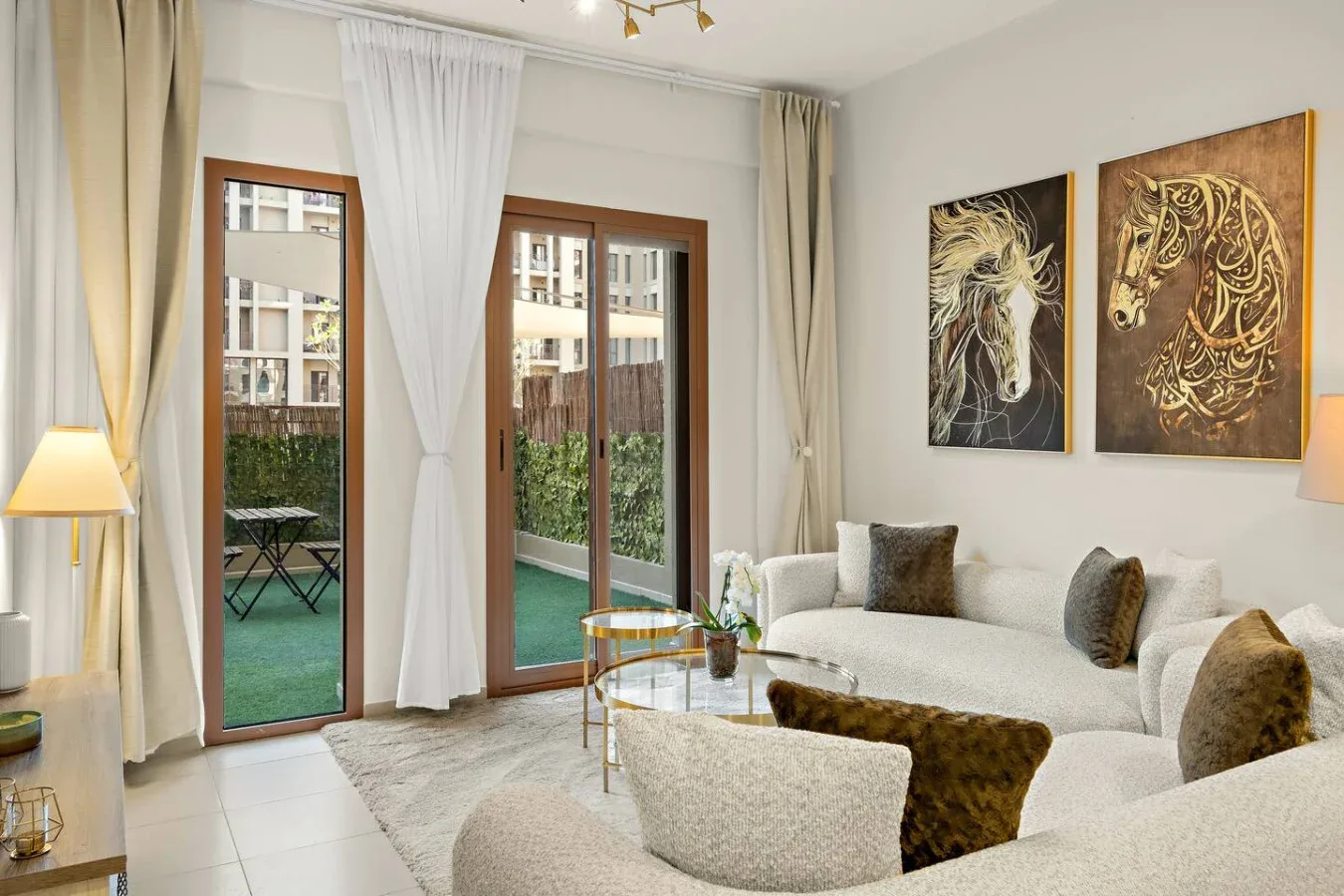 A bright living room with pale seating, tall windows, and artwork on the wall.