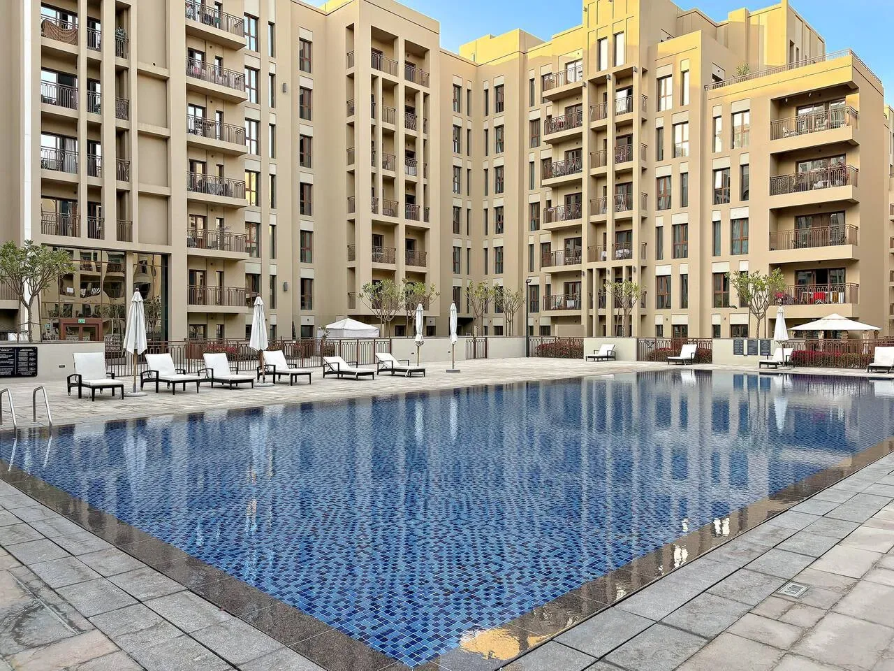A swimming pool sits in a courtyard surrounded by apartment buildings and outdoor seating.