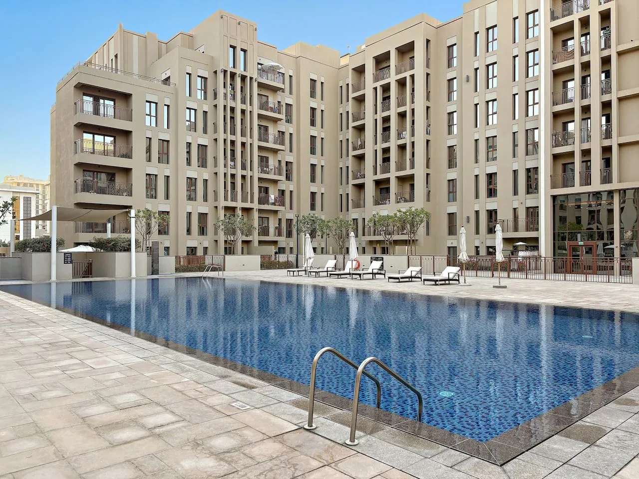A swimming pool sits beside a paved deck in front of a large apartment building.
