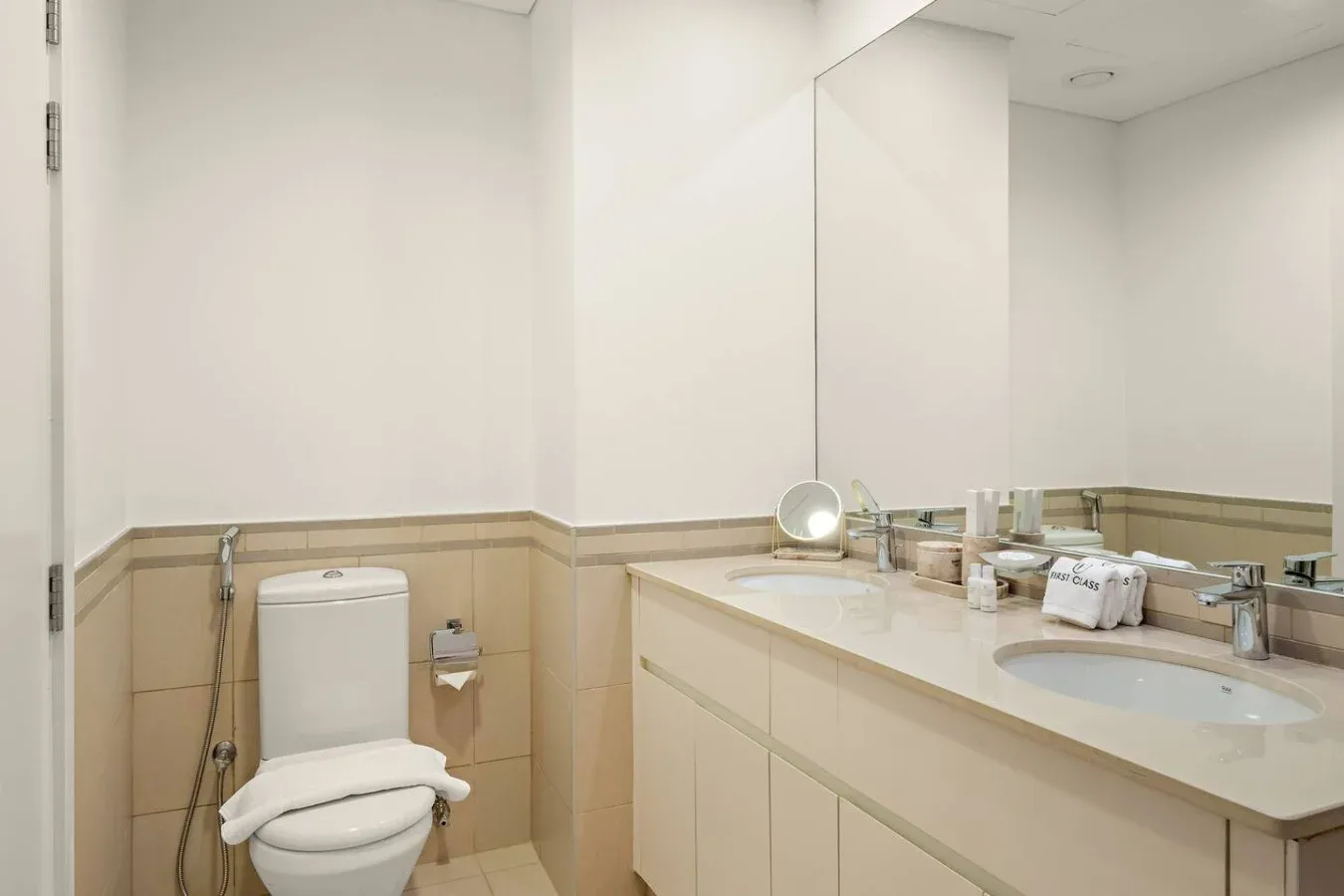 A bright bathroom with a toilet and a long sink counter beneath a large mirror.