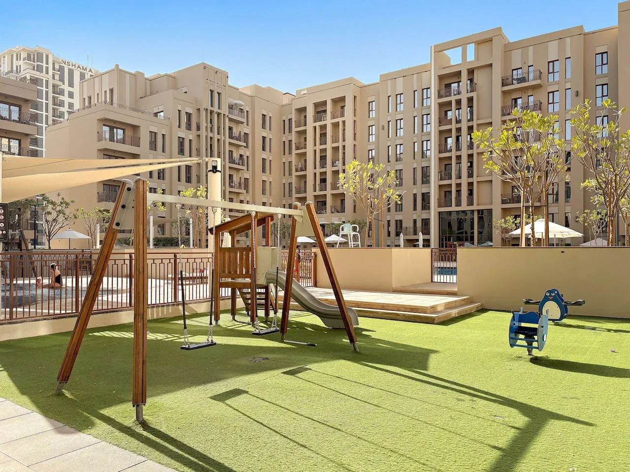 An outdoor playground with swings and a spring rider sits among apartment buildings.
