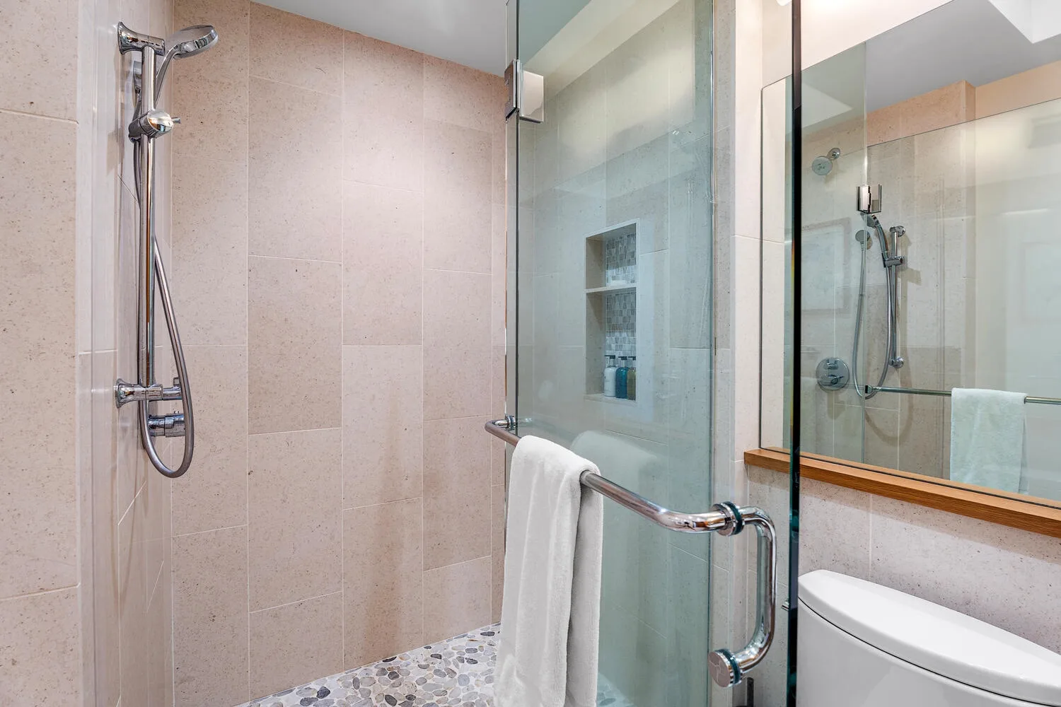 Un baño alicatado con una ducha de vidrio y una toalla colgada en el tirador.