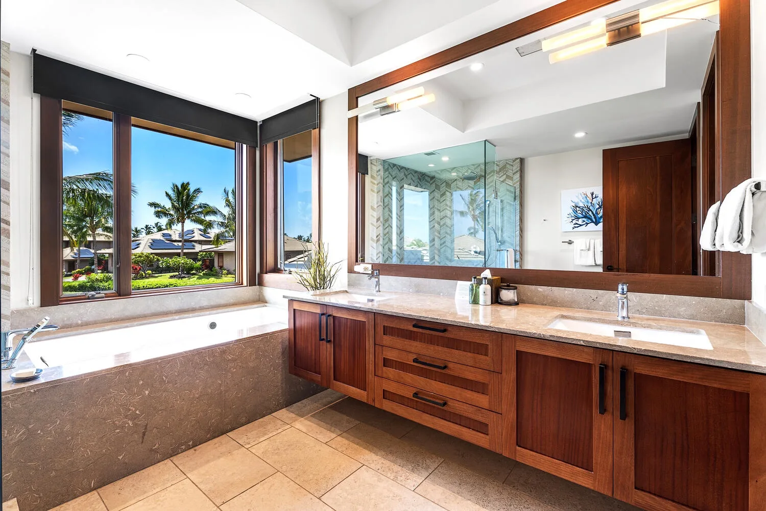 Un lavabo de baño y una bañera están junto a grandes ventanas con vista a palmeras.