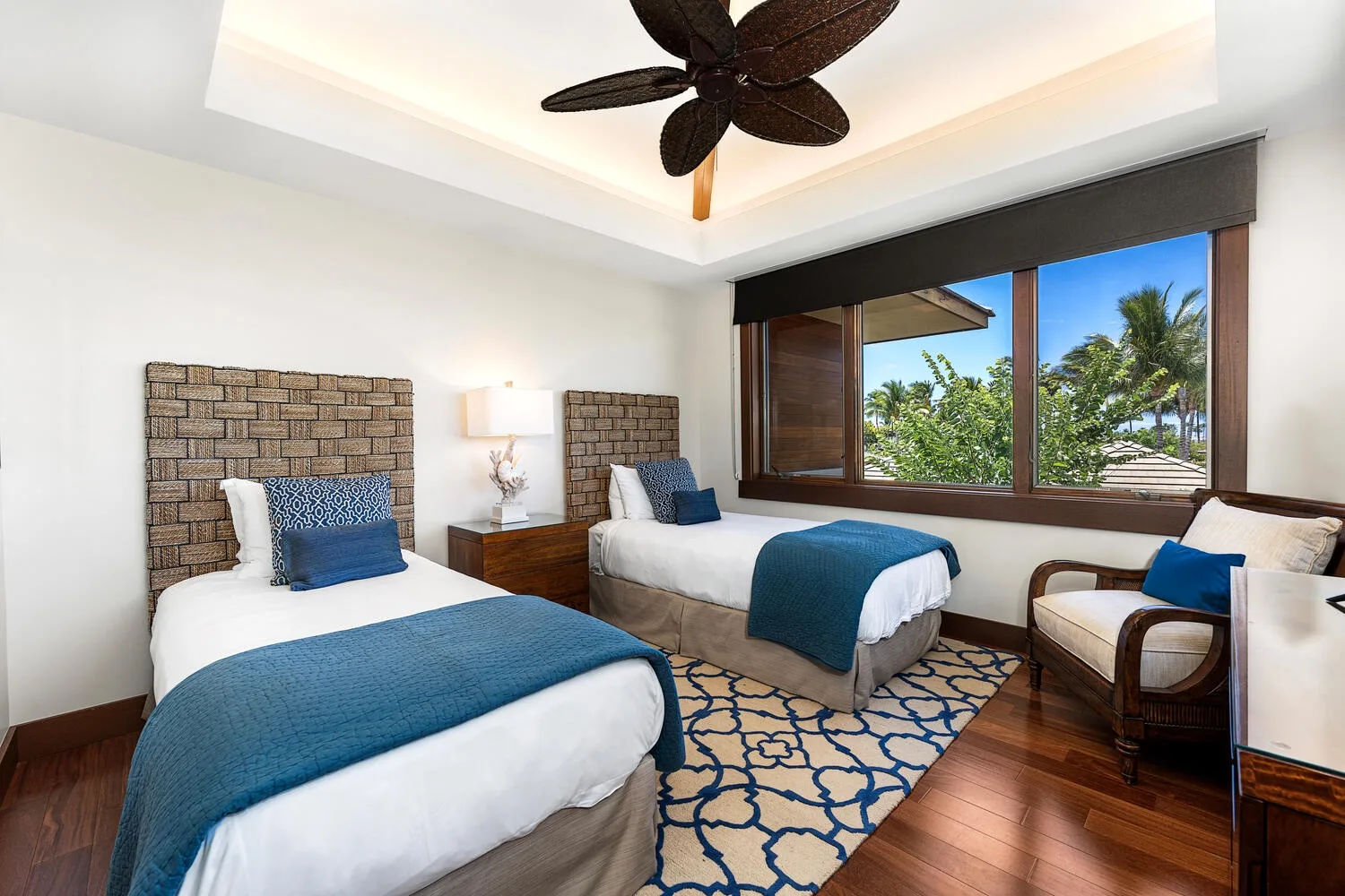 Un dormitorio luminoso con dos camas y una ventana grande con vista a palmeras.