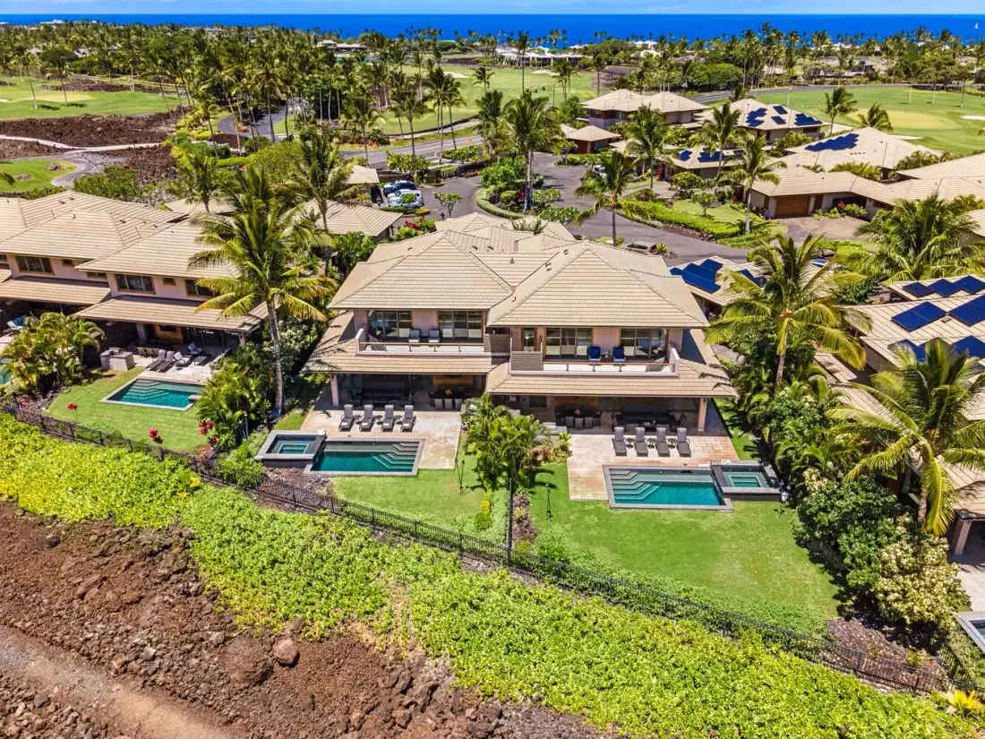 Una vista aérea muestra casas con piscinas entre jardines y palmeras.