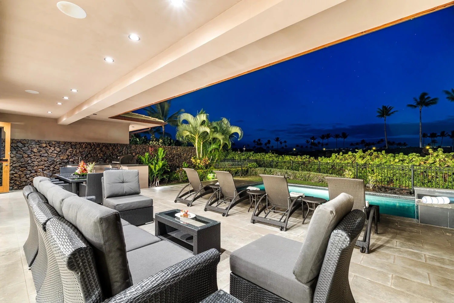 Una sala exterior cubierta se abre a una piscina y un jardín iluminado de noche.