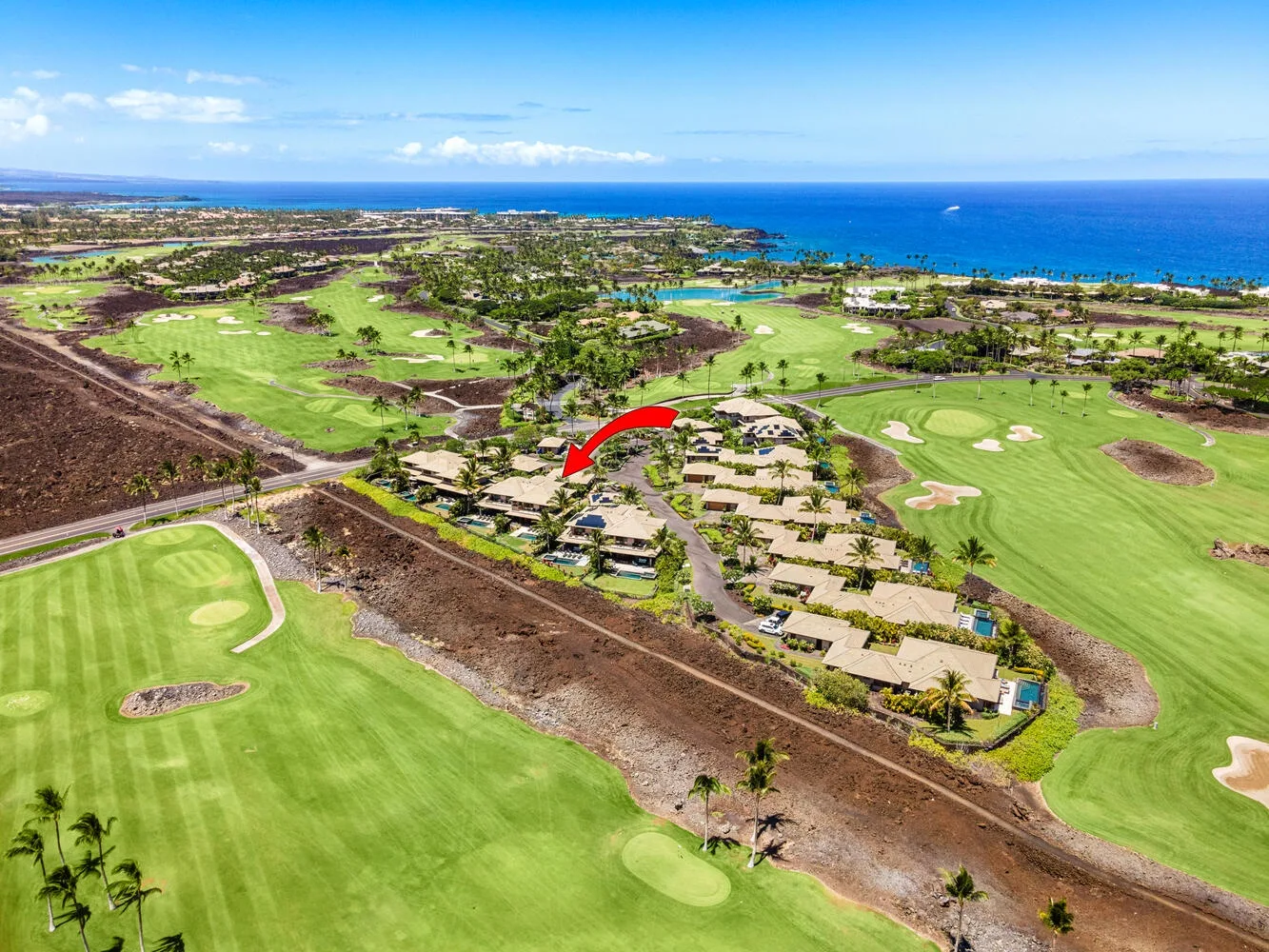 Una vista aérea muestra un campo de golf costero con calles verdes y edificios cercanos.