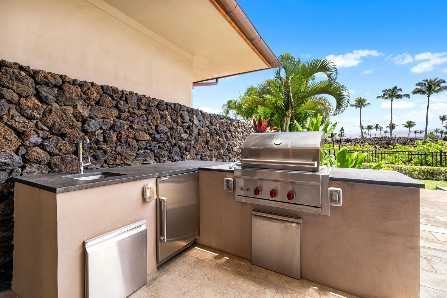 Una cocina al aire libre con parrilla empotrada y encimera junto a un muro de piedra.