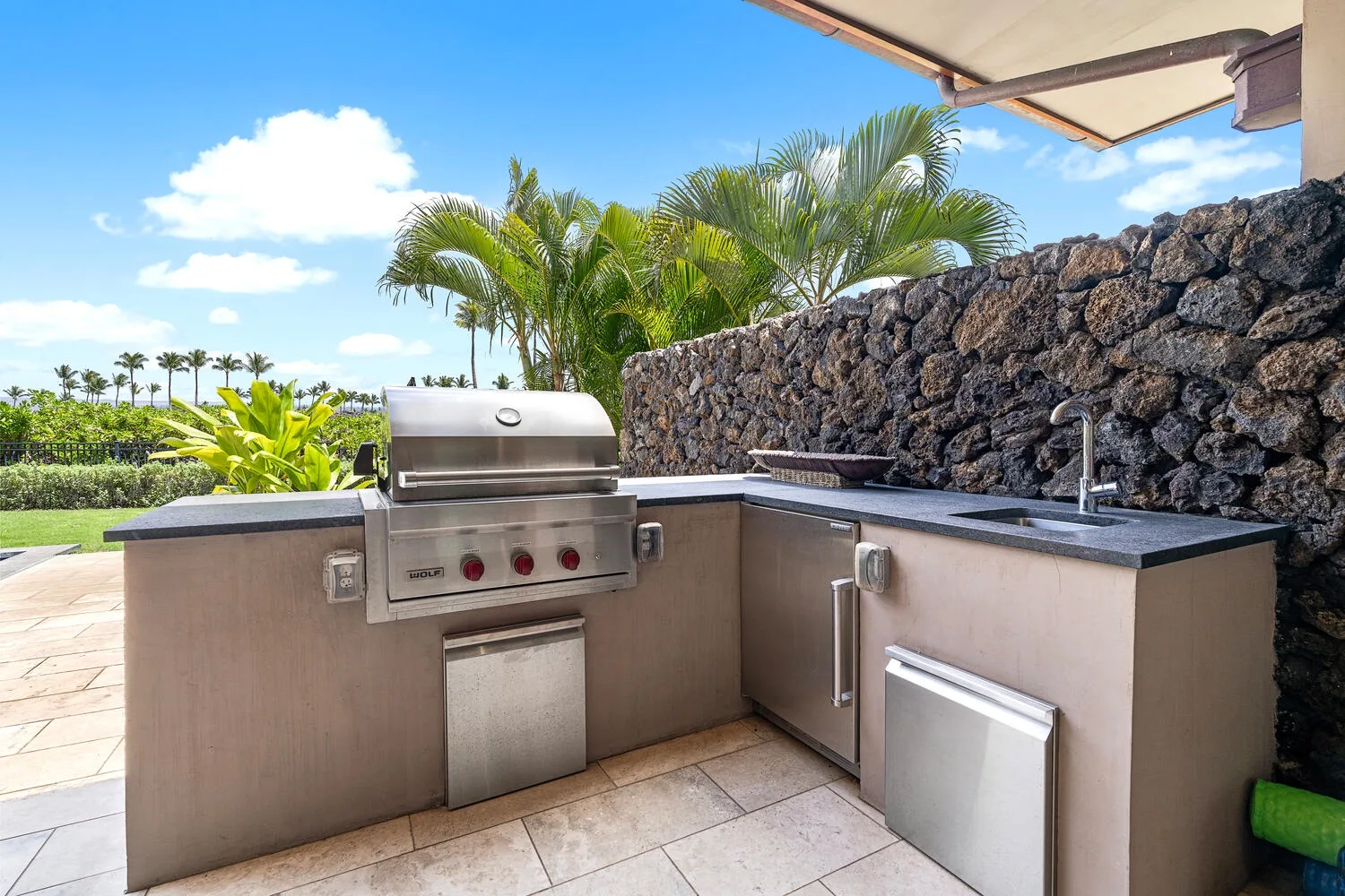 Una cocina exterior con parrilla empotrada y encimera junto a un muro de piedra.