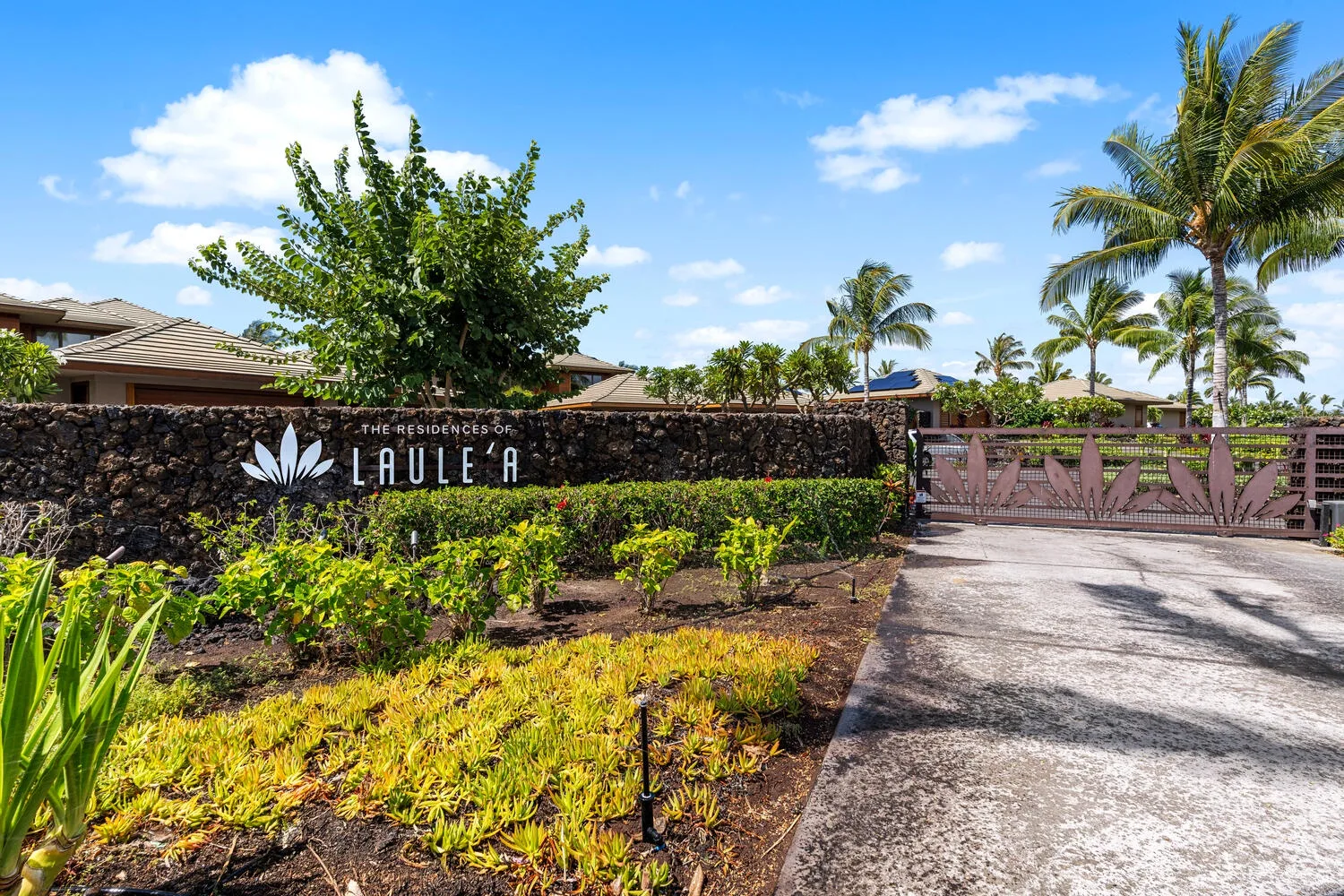 Entrada de una propiedad tropical con un muro de piedra, plantas y una entrada para vehículos.