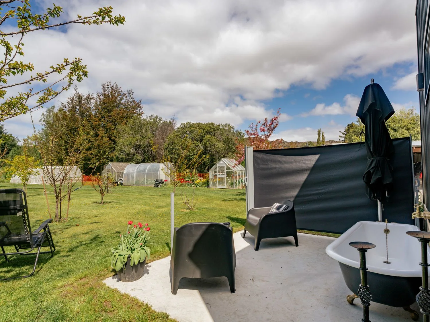 Un patio ajardinado con sillas negras, una bañera y tulipanes, con vistas a invernaderos y árboles, en Caledonia - Earnscleugh Holiday Home, en Earnscleugh